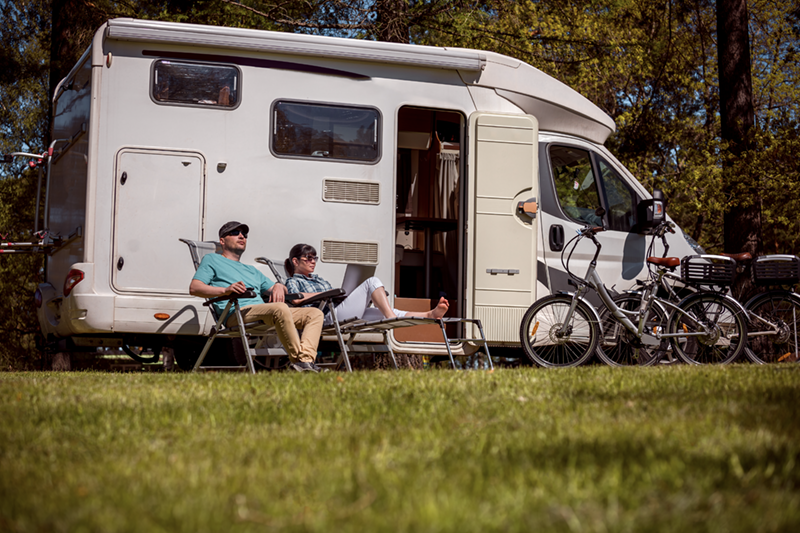 A man and woman relaxing in chairs outside their camper.